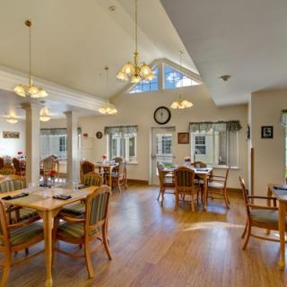 A spacious dining room with wooden tables and chairs, featuring large windows and elegant lighting.