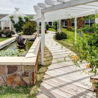 A serene garden with a shaded walkway, pergola, and pond.