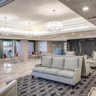 A modern and spacious hotel lobby with elegant chandeliers, comfortable sofas, and a patterned carpet.
