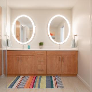 A modern bathroom with illuminated oval mirrors and wooden cabinetry.