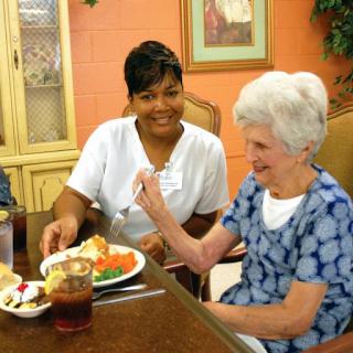 A caregiver assists an elderly woman during a meal, highlighting the importance of companionship in senior care.