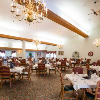 An elegant dining room with multiple tables set up and ornate chandeliers hanging from the ceiling.
