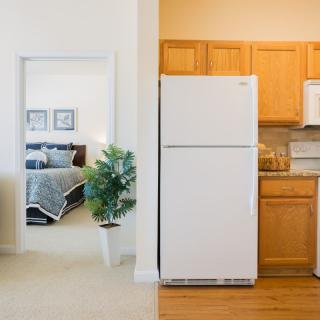 An interior view showcasing a kitchen with wooden cabinets and a white fridge adjacent to a bedroom with neutral colors.