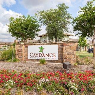 An entrance sign for a place called 'Caydance' surrounded by well-maintained landscaping, including trees and flowers.