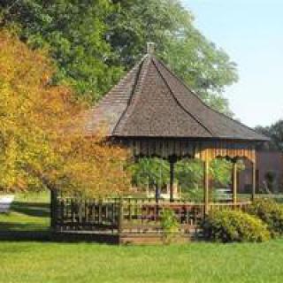 A wooden gazebo surrounded by trees and shrubs in a sunlit garden.