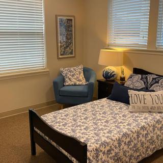 A cozy bedroom featuring a neatly made bed with patterned bedding, a blue armchair, and a warmly lit lamp.