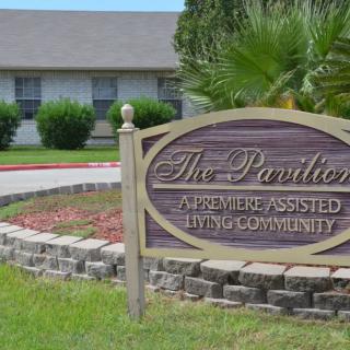 Sign for 'The Pavilion', a premiere assisted living community, set in a landscaped area with a building in the background.