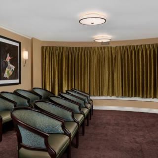 A small, elegant room with rows of chairs facing a large curtain and a painting on the wall.