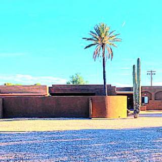 A serene desert landscape featuring a palm tree, cactus, and modern architectural structures under a bright blue sky.