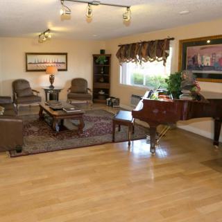 A spacious living room with hardwood flooring, featuring comfortable seating, a grand piano, and a decorative rug.