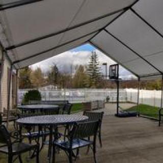 A covered patio area with tables and chairs, overlooking a backyard with a basketball hoop.