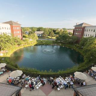 A scenic view of a pond surrounded by buildings, with tables and people gathered outdoors.