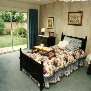 A cozy bedroom with a floral-patterned bedspread and a sliding glass door leading to the garden.