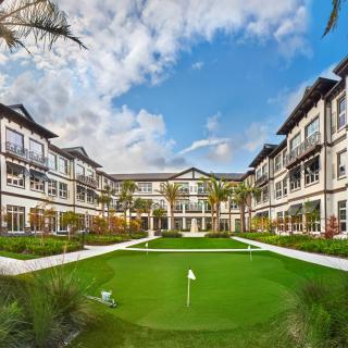 A modern residential building with a landscaped courtyard and mini golf area under a partly cloudy sky.