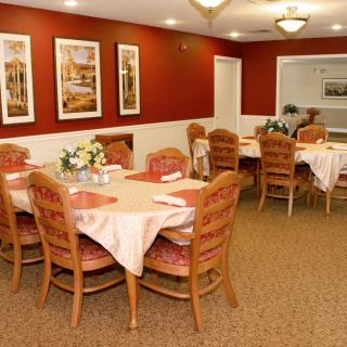 A cozy dining room with neatly set tables and warm, red walls adorned with framed paintings.
