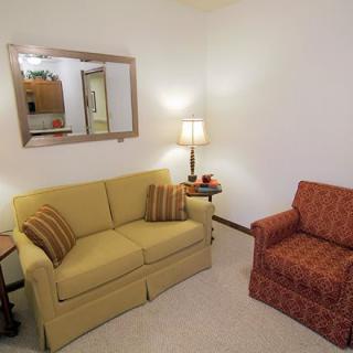 A cozy living room with a yellow sofa and orange armchair, featuring a lamp on a side table and a mirror on the wall.