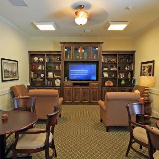 Cozy living room with a television and bookshelves, featuring comfortable chairs and elegant decor.
