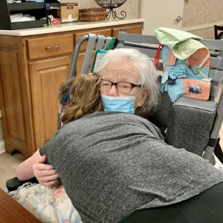 A touching moment shared between a caregiver and an elderly individual, both wearing masks for safety.