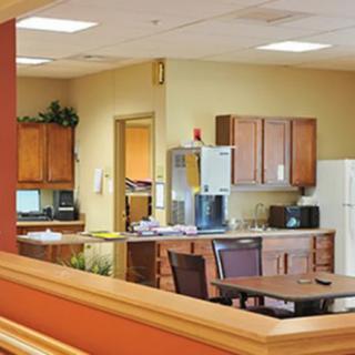 A breakroom kitchen with wooden cabinets, a refrigerator, microwave, and seating area.