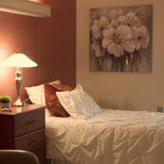 A cozy bedroom featuring a neatly made bed, a stylish lamp, and floral artwork on the wall.