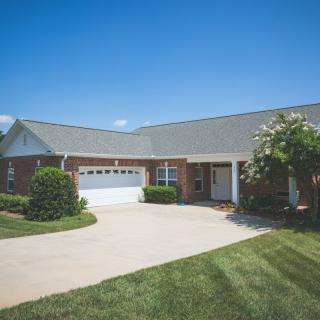 A single-story suburban house with a driveway and a well-maintained lawn under a clear blue sky.