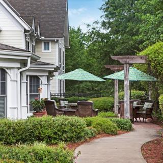 A charming outdoor patio area with seating and umbrellas next to a house, surrounded by lush greenery.