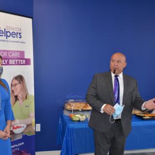 A speaker addressing an audience at a business event, with food available and promotional materials displayed.