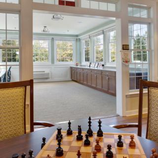 A cozy game room with a chess set ready for play, overlooking a bright sunroom.