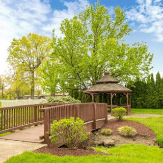 A serene park scene featuring a wooden gazebo and bridge surrounded by lush green trees.