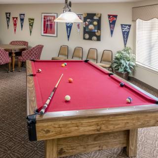 A cozy game room featuring a pool table with red felt, surrounded by chairs and decorated with pennants.