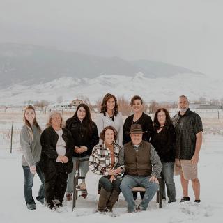 A family gathers for a group photo in a snowy outdoor setting with mountains in the background.