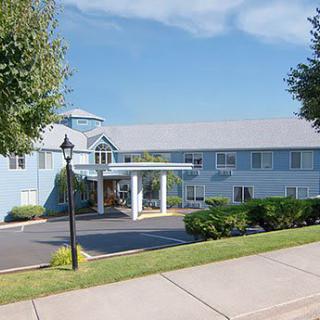 Exterior view of a hotel with a driveway and surrounding greenery under a clear blue sky.