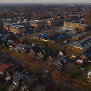 A scenic aerial view of a suburban neighborhood, showcasing residential homes and nearby buildings with a backdrop of a sunset.