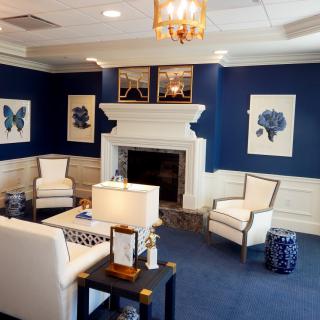 A modern living room featuring blue walls, white furniture, and elegant artwork, centered around a cozy fireplace.