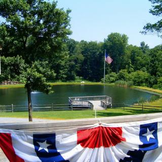 A scenic view of a lakeside with an American flag and patriotic decorations under a sunny sky.