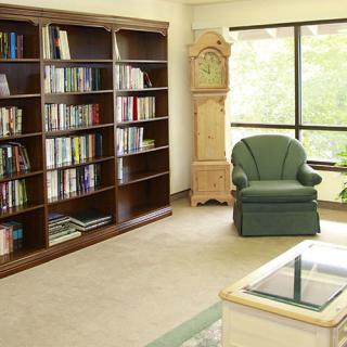 A cozy reading corner with a bookshelf, armchair, and grandfather clock by the window.