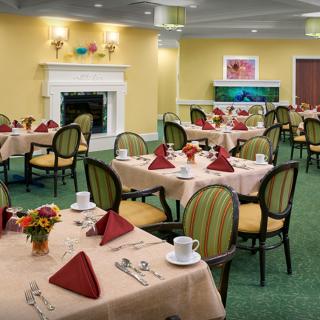 An elegant dining room with neatly set tables and chairs, featuring a cozy fireplace.