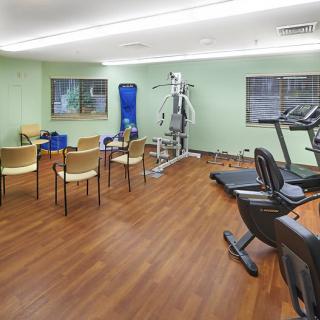A small gym with fitness equipment and chairs arranged in a clean, indoor setting.