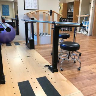 A physical therapy space featuring exercise equipment, including a barre and a patient chair.