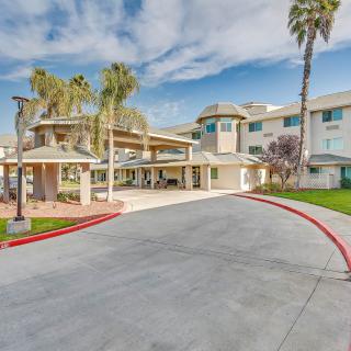 A modern building entrance with palm trees and a curved driveway under a blue sky.