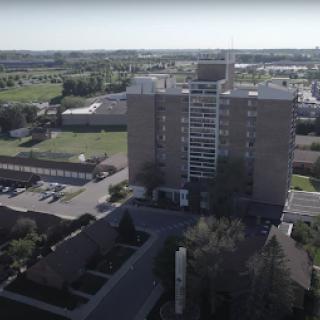 An aerial view of a multi-story building surrounded by green spaces and parking areas in an urban setting.