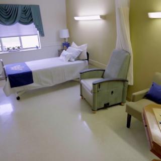 A clean and minimalist hospital room featuring a bed, an armchair, and natural light.