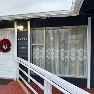 A house exterior featuring a white door with a red wreath, adjacent window with curtains, and an access ramp.