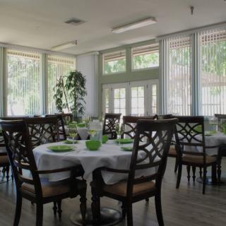 A well-lit dining area with neatly arranged tables and chairs, featuring large windows allowing natural light to fill the room.