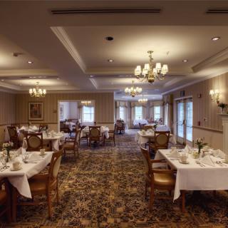 An elegant dining room with neatly arranged tables and chairs, adorned with chandeliers and a carpeted floor.