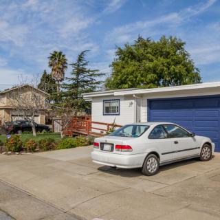 A suburban house with a blue garage and a silver car parked in the driveway on a sunny day.