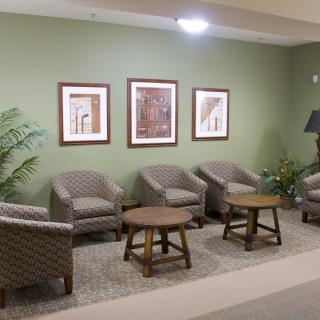 A cozy waiting area with comfortable chairs, small tables, and decorative paintings on a green wall.
