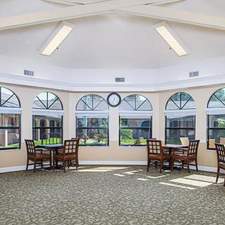 A bright room with multiple tables and chairs, large windows, and overhead lighting.