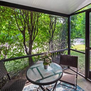 A cozy screened porch with a glass table and chairs surrounded by lush greenery.