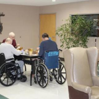 Elderly individuals in wheelchairs having a meal together in a care home setting.